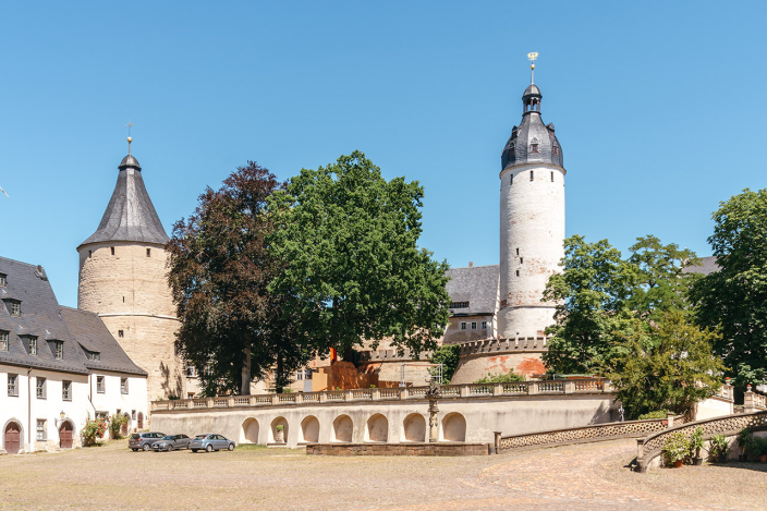 Blick vom Schlosshof auf den Agnesgarten mit Flaschenturm links und Hausmannsturn rechts. Unter blauem Himmel und mich grünbewachsenen Bäumen im Schlossgarten.